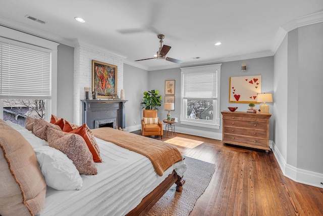 bedroom with visible vents, baseboards, a brick fireplace, crown molding, and hardwood / wood-style floors
