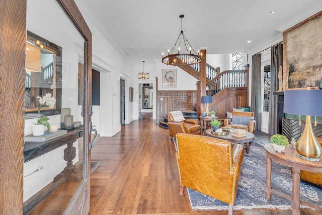 living area featuring wood finished floors, a notable chandelier, stairway, and crown molding