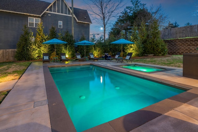 pool at dusk with a fenced in pool, a patio area, an in ground hot tub, and fence