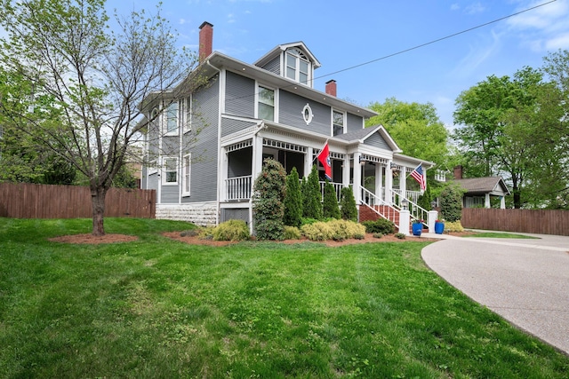 american foursquare style home with fence, a chimney, covered porch, and a front yard