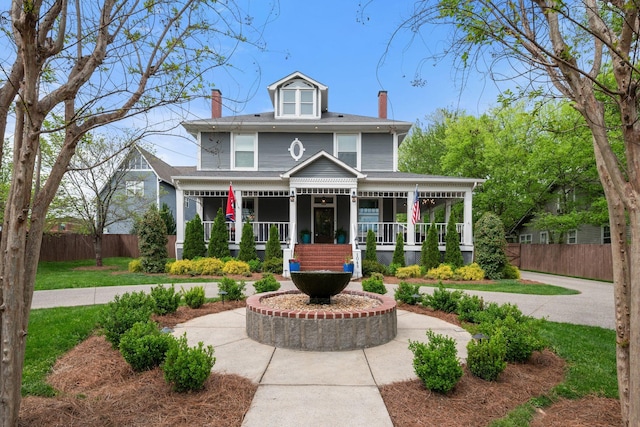 american foursquare style home featuring a porch, a chimney, and fence
