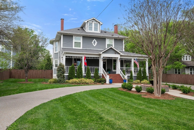 traditional style home with a chimney, a front yard, covered porch, and fence