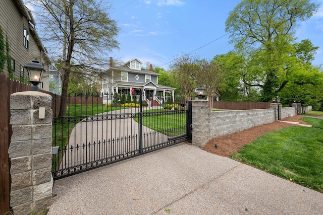 view of gate with a lawn, a porch, and a fenced front yard