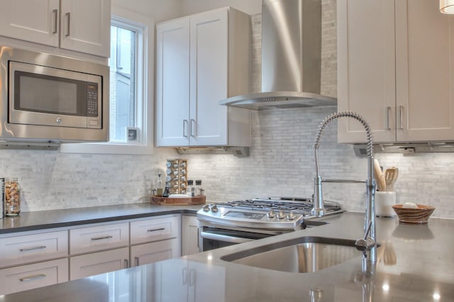 kitchen with wall chimney range hood, stainless steel microwave, tasteful backsplash, dark countertops, and white cabinetry
