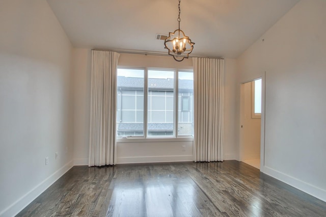 spare room featuring a chandelier, dark wood-type flooring, and baseboards