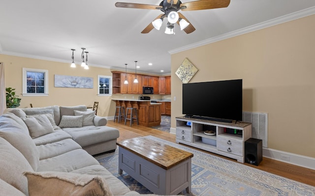 living area featuring visible vents, baseboards, ornamental molding, ceiling fan, and wood finished floors
