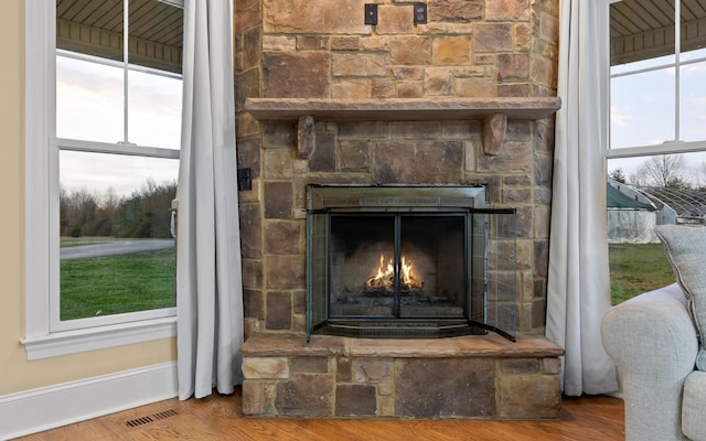 details featuring visible vents, a stone fireplace, wood finished floors, and baseboards