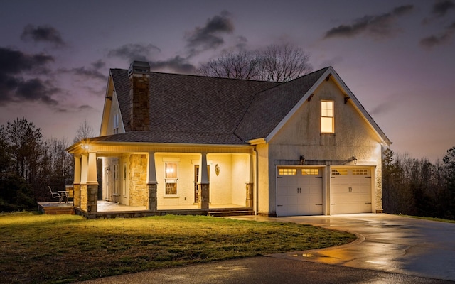 view of front of home with concrete driveway, stucco siding, a chimney, a yard, and covered porch