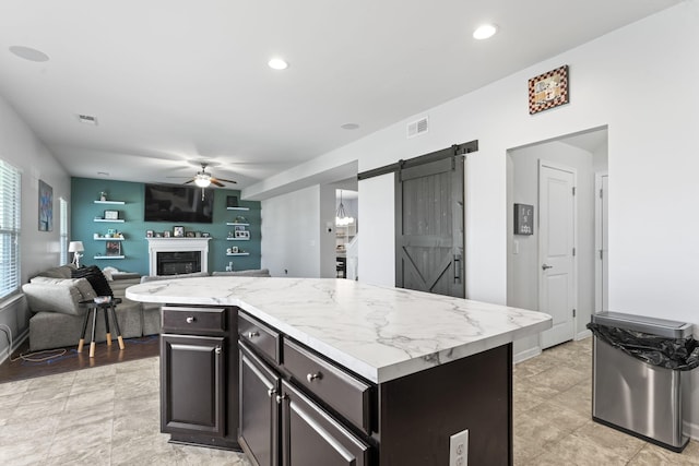 kitchen featuring visible vents, a barn door, a ceiling fan, and a fireplace