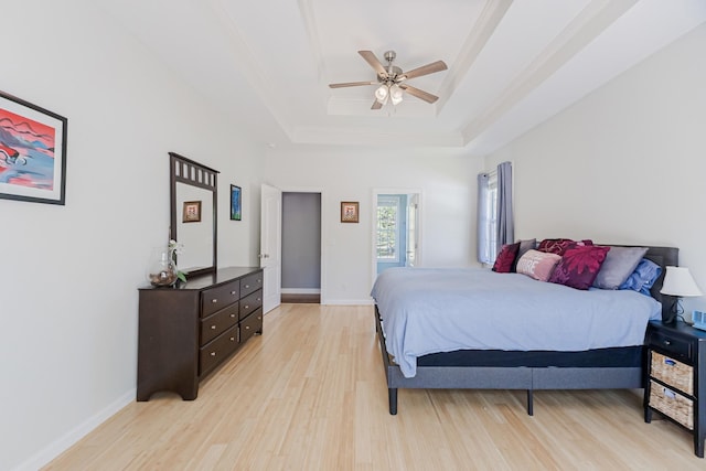 bedroom featuring a tray ceiling, light wood-style floors, ceiling fan, and baseboards