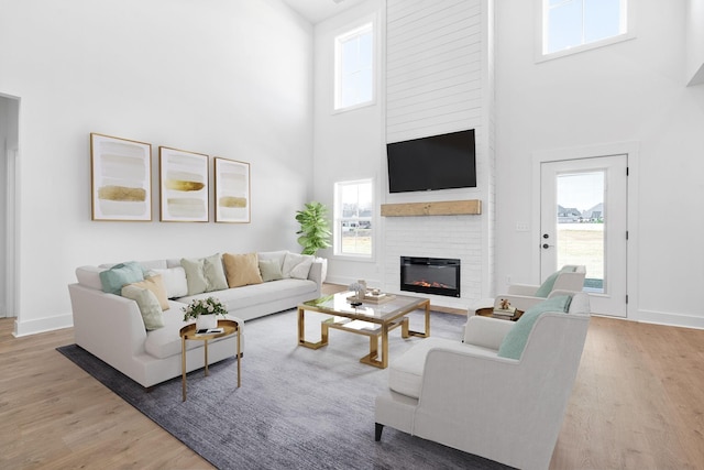 living room featuring wood finished floors, a fireplace, a towering ceiling, and baseboards
