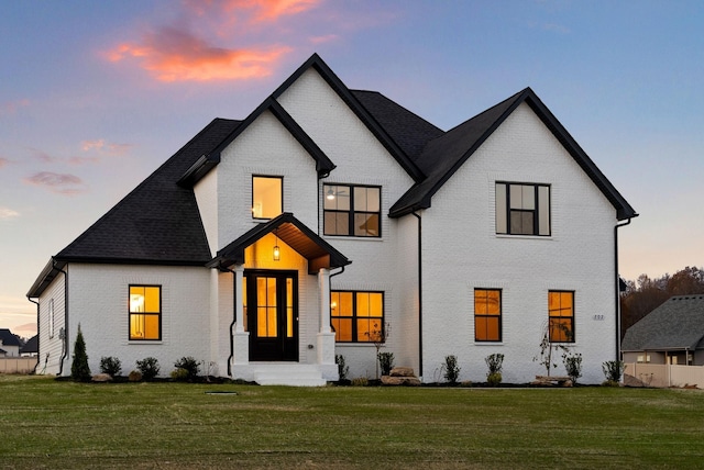 back of house at dusk with a yard and brick siding