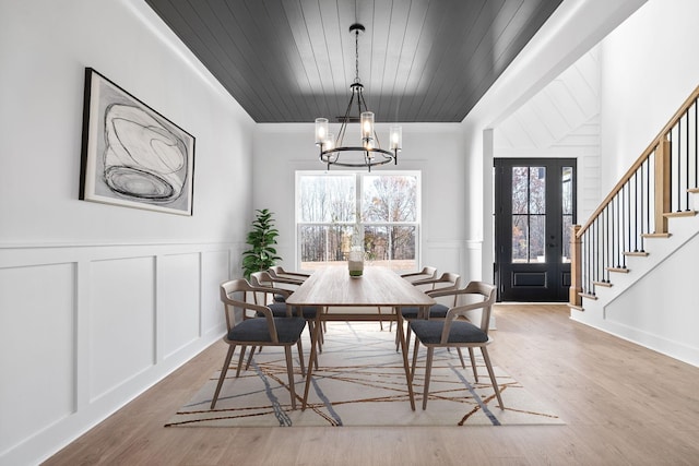 dining space featuring a decorative wall, an inviting chandelier, wood finished floors, and stairs