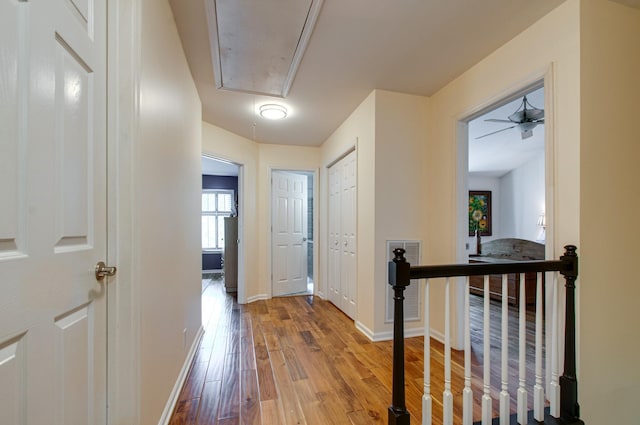 hall featuring baseboards, attic access, and wood finished floors
