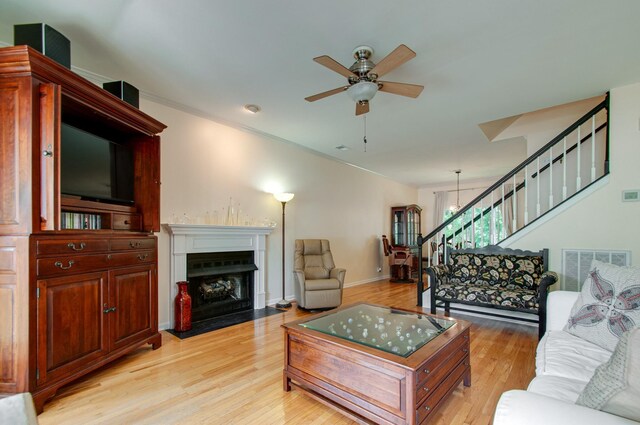living area with visible vents, ceiling fan, light wood-type flooring, a fireplace with flush hearth, and stairs