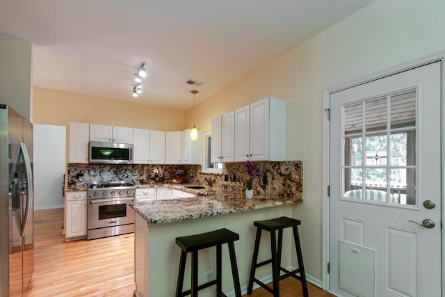 kitchen featuring visible vents, appliances with stainless steel finishes, light wood-style floors, a peninsula, and light stone countertops