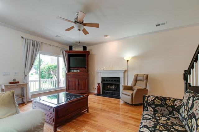 living room with a fireplace with flush hearth, ornamental molding, a ceiling fan, and light wood finished floors