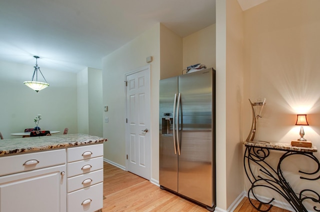 kitchen featuring stainless steel fridge with ice dispenser, light stone countertops, white cabinetry, hanging light fixtures, and light wood finished floors