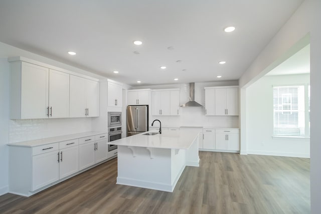 kitchen featuring wall chimney range hood, a sink, appliances with stainless steel finishes, light wood finished floors, and backsplash