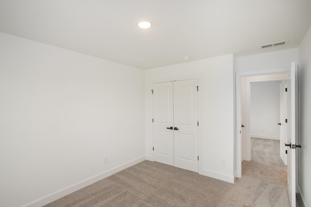 unfurnished bedroom featuring light colored carpet, visible vents, a closet, and baseboards