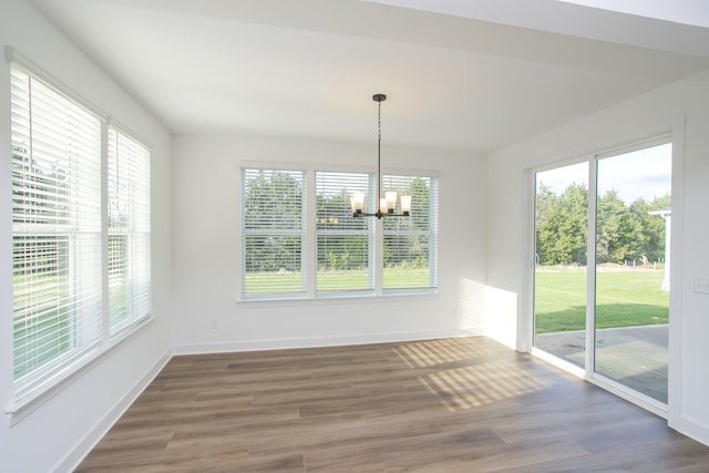 unfurnished dining area with an inviting chandelier, a wealth of natural light, and wood finished floors