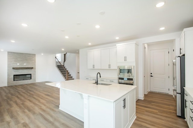 kitchen featuring a kitchen island with sink, light wood finished floors, a sink, stainless steel appliances, and light countertops
