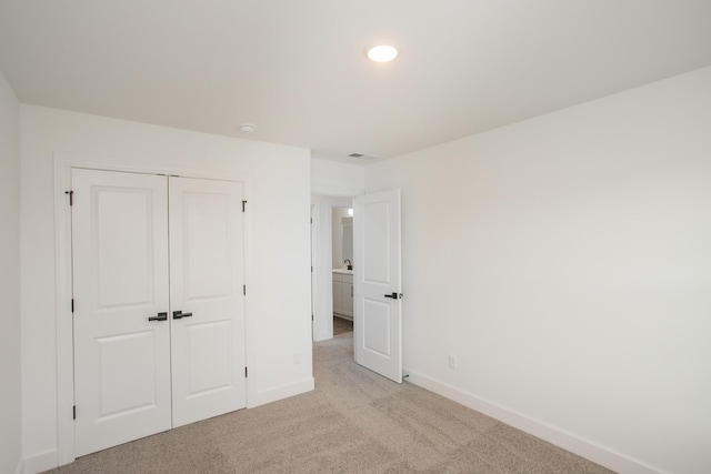 unfurnished bedroom with a closet, visible vents, light carpet, and baseboards