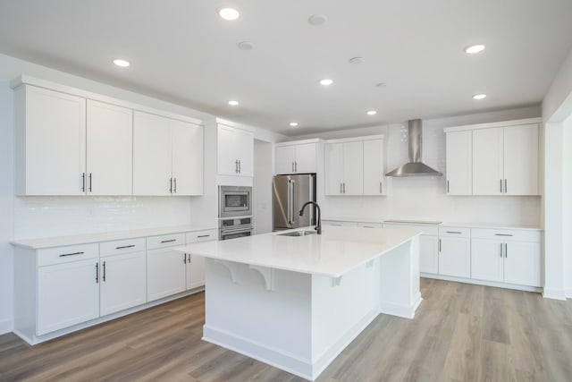 kitchen featuring tasteful backsplash, wall chimney exhaust hood, appliances with stainless steel finishes, and light wood-style flooring