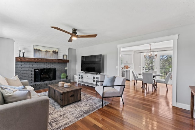 living room with wood finished floors, ceiling fan with notable chandelier, a fireplace, and baseboards