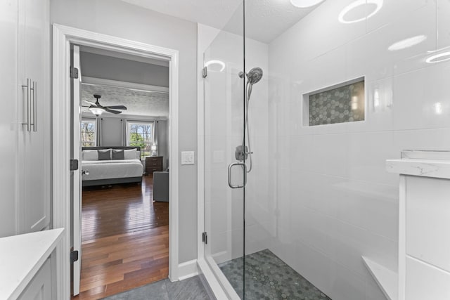 ensuite bathroom with a ceiling fan, a shower stall, vanity, ensuite bath, and wood finished floors