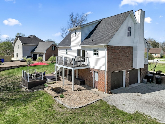 rear view of house featuring an attached garage, a lawn, brick siding, a wooden deck, and driveway