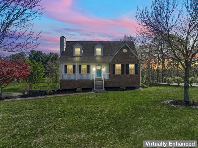cape cod home with covered porch, a lawn, roof with shingles, brick siding, and a chimney