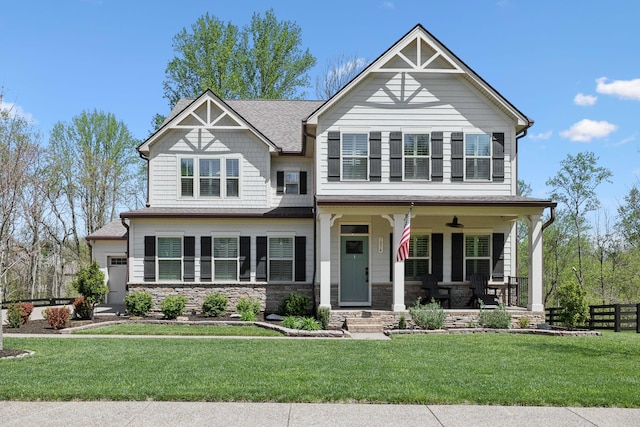 craftsman-style house with a front yard, a porch, stone siding, and fence