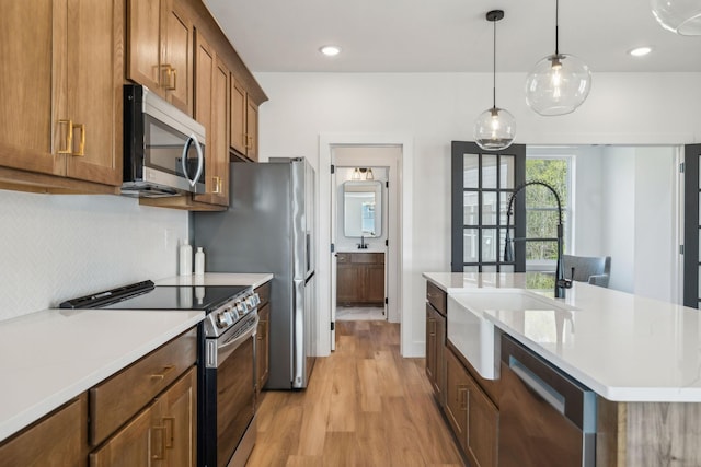 kitchen with light countertops, light wood finished floors, a kitchen island with sink, and stainless steel appliances
