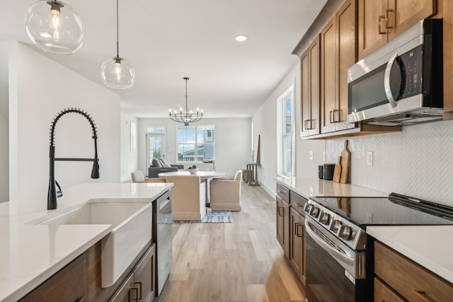 kitchen with appliances with stainless steel finishes, light wood-style flooring, decorative backsplash, pendant lighting, and a sink