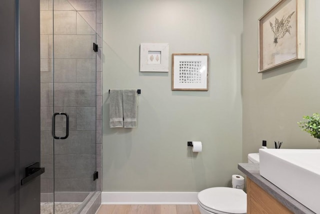 bathroom with baseboards, toilet, a shower stall, vanity, and wood finished floors