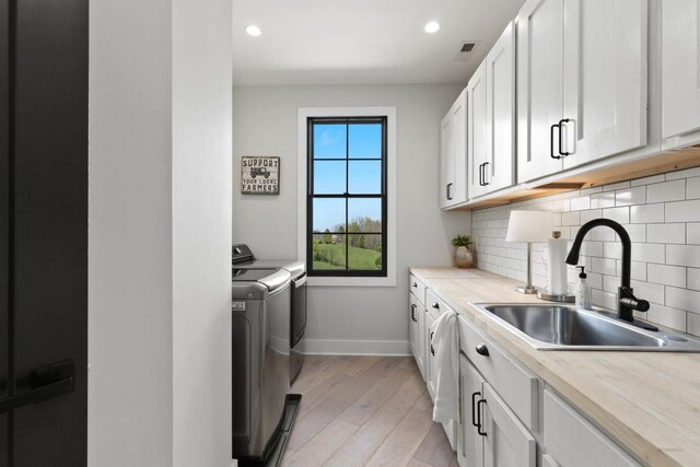 clothes washing area with light wood-style flooring, a sink, baseboards, cabinet space, and washer and clothes dryer