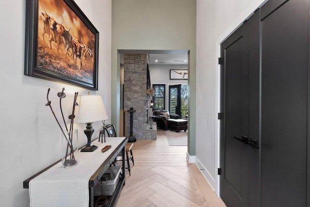hall with light wood-type flooring, a high ceiling, and baseboards