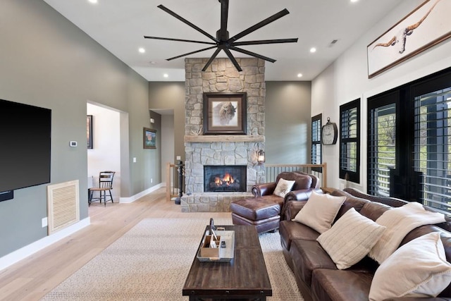 living area featuring a fireplace, a ceiling fan, visible vents, wood finished floors, and baseboards