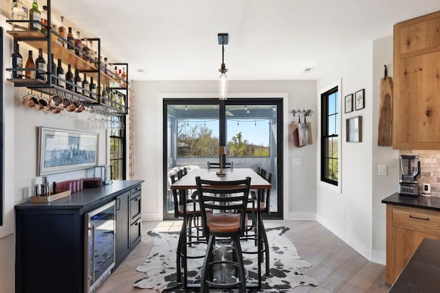 dining room with light wood-style floors, wine cooler, baseboards, and indoor bar