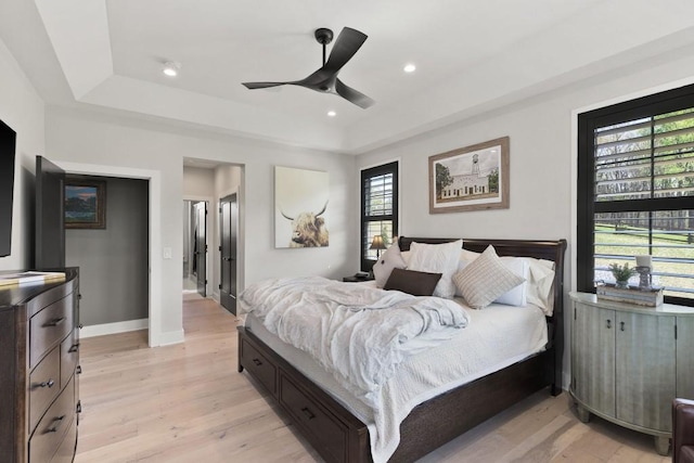 bedroom with a raised ceiling, baseboards, and light wood-style flooring