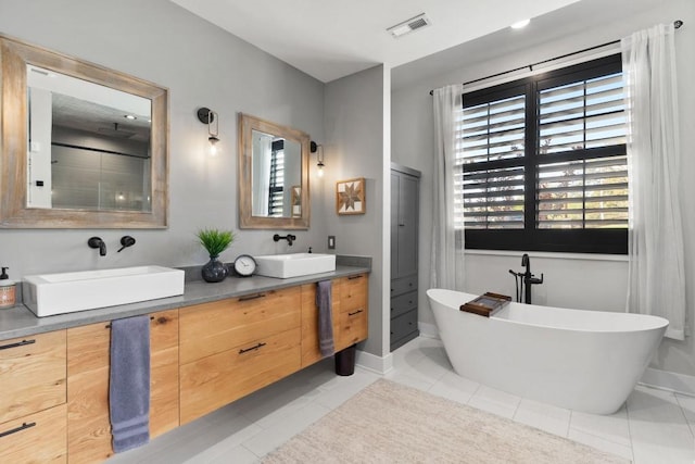 bathroom featuring baseboards, a freestanding tub, a sink, and visible vents