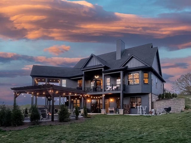 rear view of property featuring a patio, a balcony, a chimney, board and batten siding, and a yard