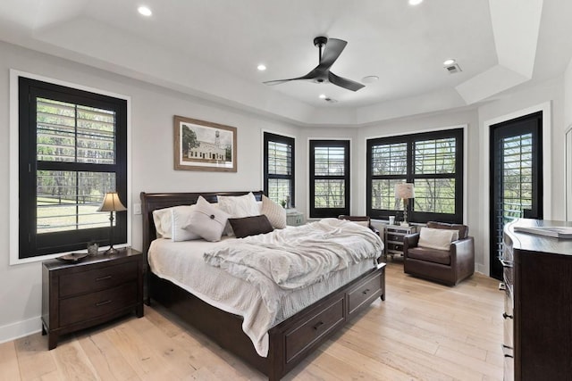 bedroom featuring light wood-style flooring, multiple windows, baseboards, and a raised ceiling