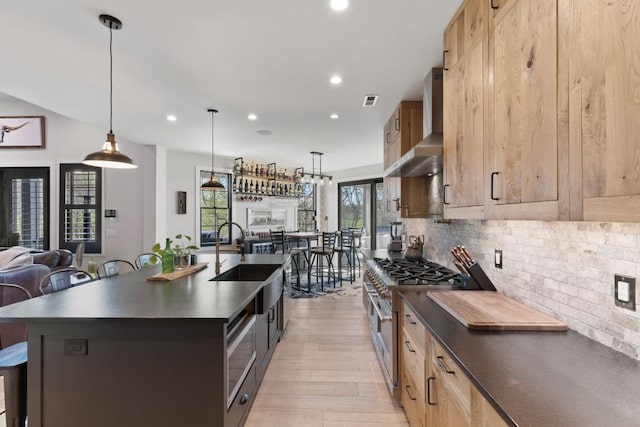kitchen with stainless steel range, wall chimney range hood, a sink, dark countertops, and light wood-style floors