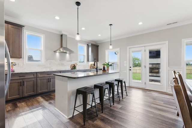 kitchen featuring dark stone counters, dark wood-style flooring, wall chimney range hood, and a healthy amount of sunlight