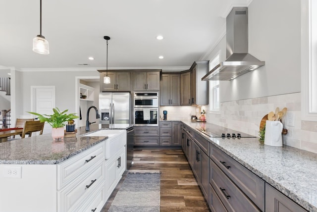 kitchen with light stone counters, stainless steel appliances, wall chimney range hood, ornamental molding, and a sink