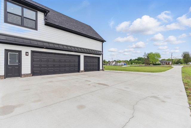 view of property exterior with driveway, a standing seam roof, metal roof, an attached garage, and a lawn