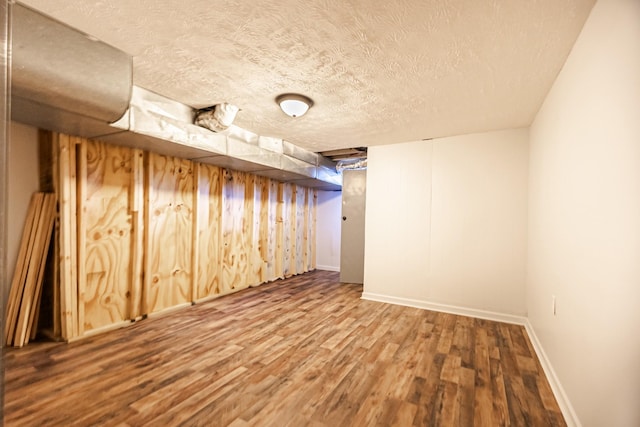 finished below grade area featuring a textured ceiling, wood finished floors, and baseboards