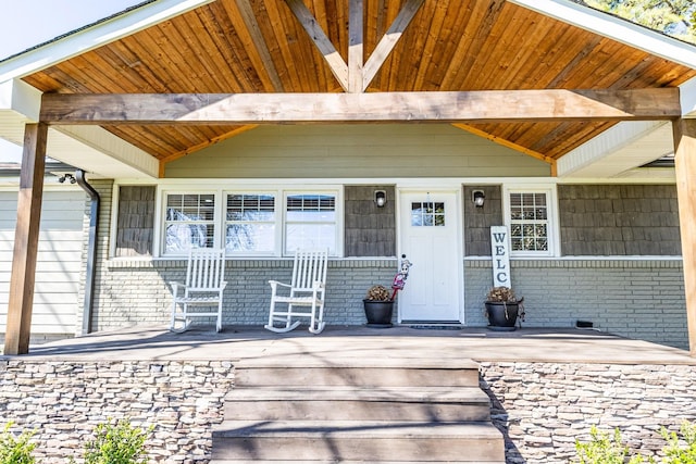 view of exterior entry with crawl space, covered porch, and brick siding